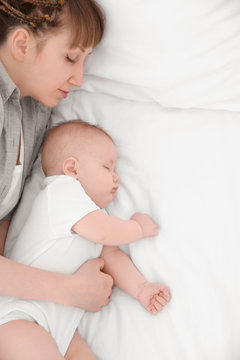 Young woman with cute baby sleeping on bed at home