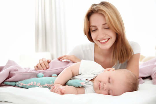 Young woman with cute sleeping baby lying on bed at home