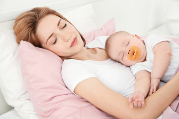 Young woman with cute baby sleeping on bed at home