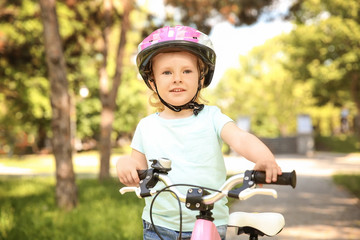 Naklejka premium Cute little girl with bicycle in park on sunny day