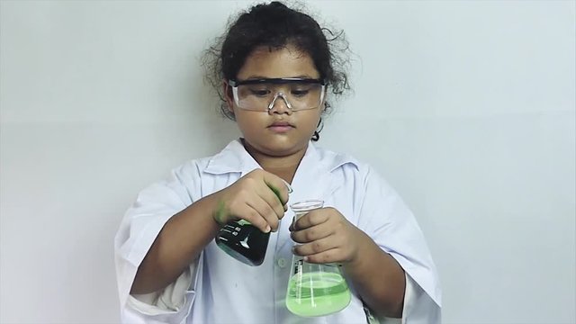 Medium close up of a multicultural ethnic girl pouring green fluid into a science beaker in semi-slow motion (50fps); fluid bubbles up, to her surprise.  - Powered by Adobe