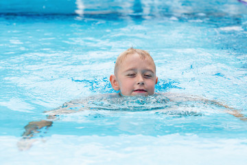 Fototapeta na wymiar A cute blond boy learning to swim in a swimming pool