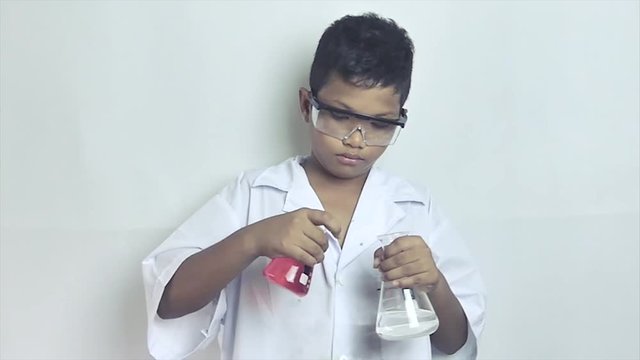 Slow motion medium shot of a multicultural ethnic boy pouring a bubbling mixture into a science beaker - he then makes an amazed and surprised reaction.