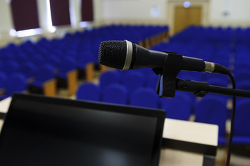 Microphone in conference hall, auditorium for business meeting and presentation with rostrum and display for speaker and rows of seats for participants and visitors on blurred background 