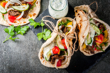 Healthy snack, lunch. Traditional Greek wrapped sandwich gyros - tortillas, bread pita with a filling of vegetables, beef meat and sauce tzatziki. On black stone table Copy space