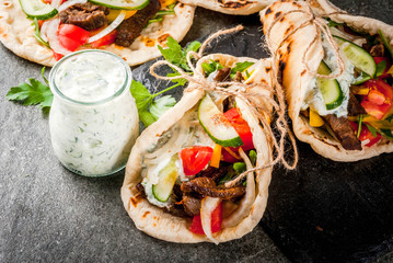 Healthy snack, lunch. Traditional Greek wrapped sandwich gyros - tortillas, bread pita with a filling of vegetables, beef meat and sauce tzatziki. On black stone table Copy space - obrazy, fototapety, plakaty