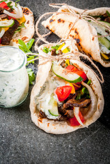 Healthy snack, lunch. Traditional Greek wrapped sandwich gyros - tortillas, bread pita with a filling of vegetables, beef meat and sauce tzatziki. On black stone table Copy space