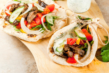 Healthy snack, lunch. Traditional Greek wrapped sandwich gyros - tortillas, bread pita with a filling of vegetables, beef meet and sauce tzatziki. On light stone table Copy space