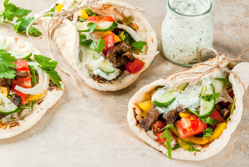 Healthy snack, lunch. Traditional Greek wrapped sandwich gyros - tortillas, bread pita with a filling of vegetables, beef meat and sauce tzatziki. On light stone table Copy space top view
