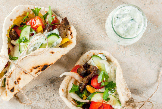 Healthy snack, lunch. Traditional Greek wrapped sandwich gyros - tortillas, bread pita with a filling of vegetables, beef meat and sauce tzatziki. On light stone table Copy space top view