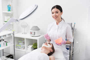 Cheerful beautician is holding brush and bowl