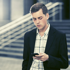 Young handsome business man using smart phone walking in city street