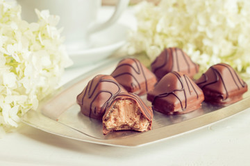 Chocolate sweets with a stuffing on an iron plate and white flowers on a wooden light background.