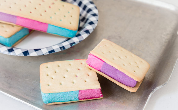 horizontal image of ice cream sandwiches with blue and pink and purple ice cream stuck between the biscuits 