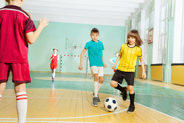 Boy striking ball playing football in sports hall
