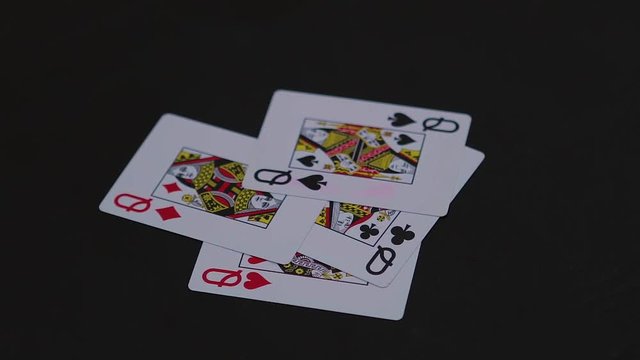 Four queen poker cards falling on the black table