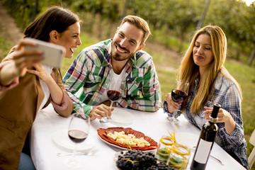 Young people sitting by the table and drinking red wine in the vineyard