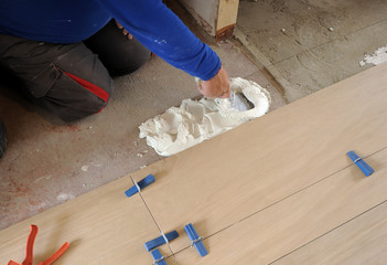 Bricklayer spreading white cement with trowel to place a new porcelain tile floor in the living...