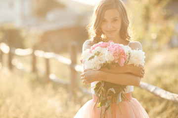 Beautiful young girl with peony on the nature outdoors in the sunshine. Pretty woman outside with...