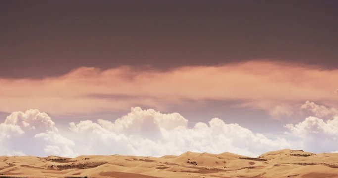 4k timelapse large white puffy cloud mass rolling over desert sand dunes under sunset glow. 	
