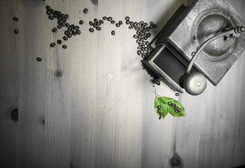 Fototapeta na wymiar telling story from the past - grinding roasted beans of coffee with old vintage retro grinder with ground coffee and green leaf in black and white top view on wooden background with copy space 