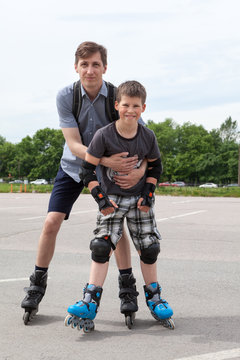 Father holding son while riding on roller-skates in city park