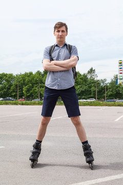 Confident European young man standing in roller-skates on asphalt urban road, full-lenght portrait