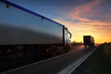 Fototapeta na wymiar Two white truck driving through autumn landscape at sunset