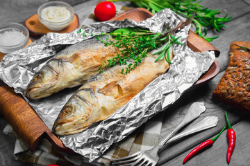 Grilled whole trout on an aluminum foil on a wooden log