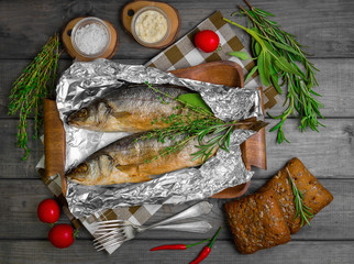 Grilled whole trout on an aluminum foil on a wooden log
