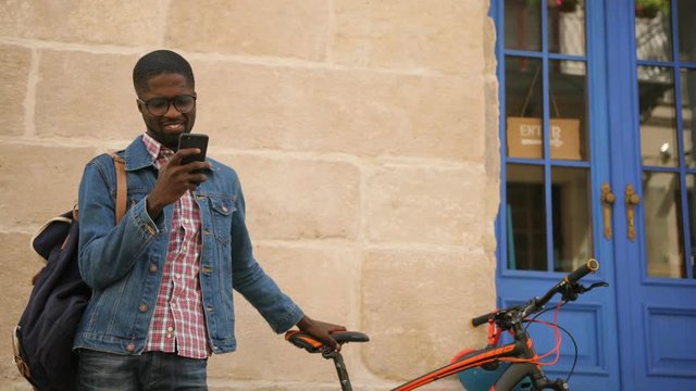 Attractive young african man using GPRS on the smart phone for choosing the best way of trip on the bicycle.