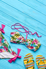 Modern bathing clothing, top view. Sandals and floral swimsuit, blue background.