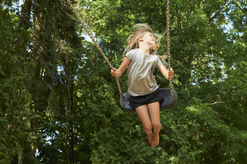 Little child blond girl having fun on a swing outdoor. Summer playground. Girl swinging high. Young...