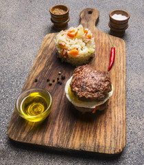 appetizing burger only meat and eggs and butter, with rice and vegetables, and spices on vintage cutting board