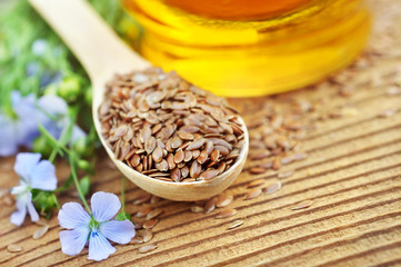 Flax seeds in spoon with linseed oil and blue linum plants, wooden background