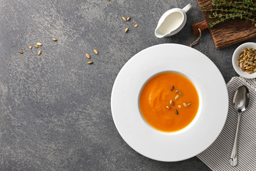 Pumpkin soup with seeds in a big white plate on gray stone background