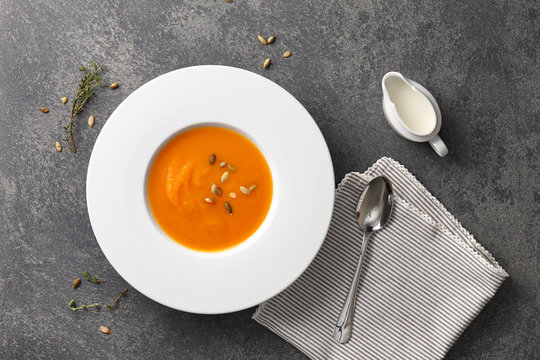 Pumpkin soup with seeds in a big white plate on gray stone background