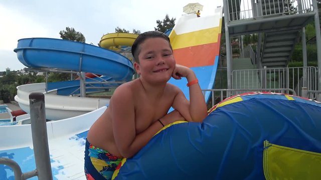 Portrait of cute teen boy in the swimming pool at aquapark looking at the camera and smiling