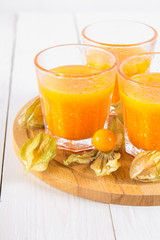 An orange smoothie made of physalis on a white wooden table.