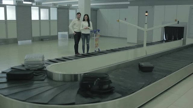 Young woman and man pick their luggage out of the luggage belt