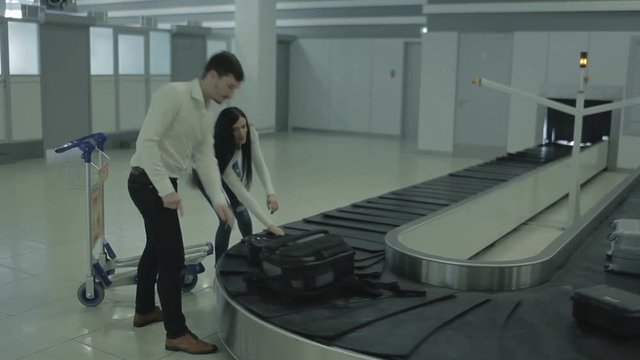 Two young people wait their baggage near the baggage claim desk in airport