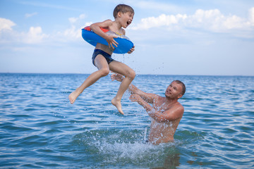 Dad and son bathe in the sea, play fun. Dad throws his son into the water.
