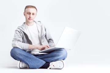 Portrait of Serious Handosme Blond Caucasian Man Sitting with Laptopp on Legs. Posing Against White Background.