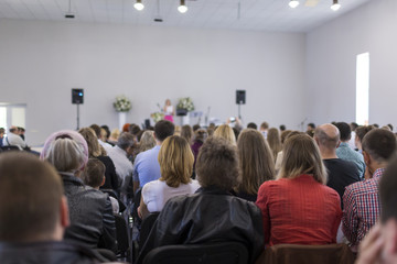 People Sitting In Lines During a Conference While Female Host Speaking on Stage