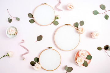 Embroidery frames with beige rose flower buds and eucalyptus on pale pastel pink background. Flat lay, top view decorated concept.