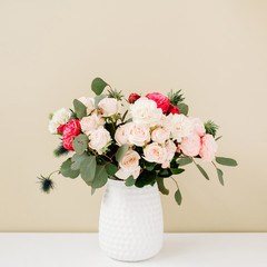 Beautiful flowers bouquet: bombastic roses, blue eringium, eucalyptus branches in flowerpot at pale pastel beige wall. Floral lifestyle composition.