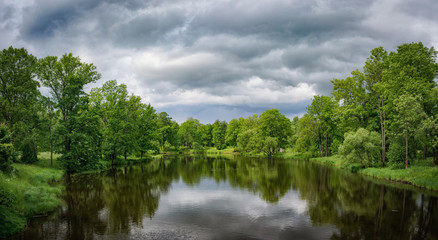 Green trees and river on a background of a cloudy sky. Panorama, reflection.