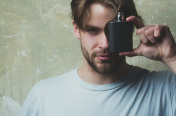 man covering eye with black perfume bottle