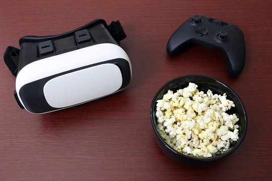 Virtual reality headset goggles sitting next to bowl of popcorn and generic remote controller