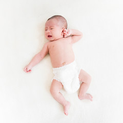 Adorable little newborn baby wearing diaper lying on the bed